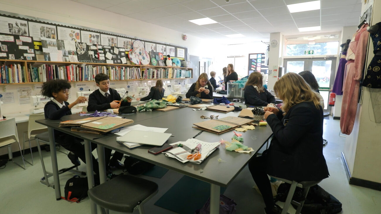 A group of school kids sat at a large table in an art class.